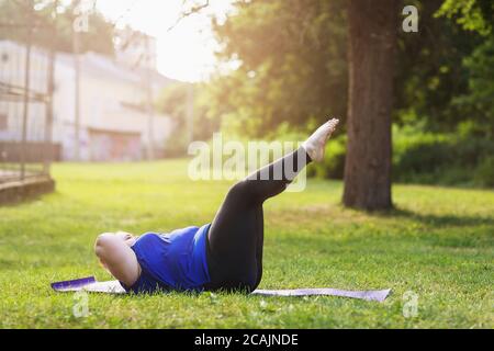 Young blonde size plus performs exercises for abdominal muscles in the park. The concept of a healthy lifestyle Stock Photo