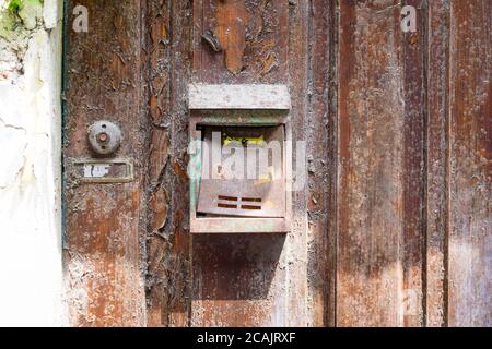 an old, worn, rusted and unlabeled mailbox, mounted on an old weathered wooden door. Next to it is an unlabeled bell. Stock Photo