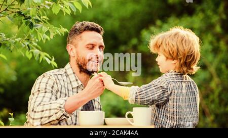 Natural nutrition concept. Feeding son natural foods. Stage of development. Feed son solids. Dad and boy eat and feed each other outdoors. Ways to develop healthy eating habits. Feed your baby. Stock Photo