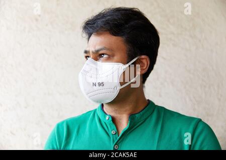 Adult Indian man wearing White N95 Mask in Green polo t-shirt looking into the camera with head faced 45 degrees and eyes looking upward Stock Photo