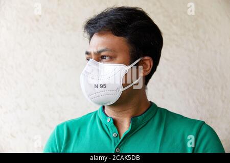 Adult Indian man wearing White N 95 Mask in Green round neck t-shirt looking into the camera with head faced 45 degrees against a textured wall Stock Photo