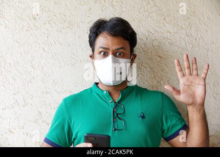 A man wearing a Green T-shirt holds a cell phone while looking surprised Stock Photo