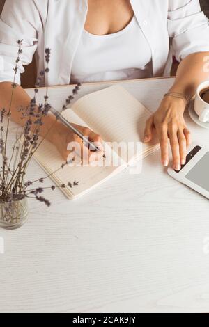 A woman writes in a notebook while sitting in the room at the table. Stock Photo