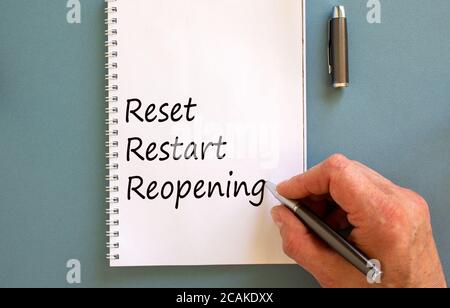 Male hand writing 'reset, restart, reopening' on white note, isolated on blue background. Stock Photo