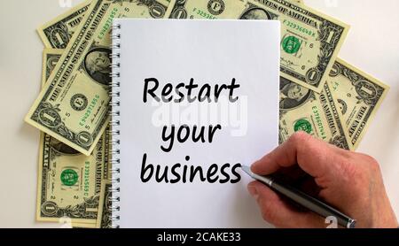 Male hand writing 'restart your business' on white note, on white background. Dollar bills. Stock Photo