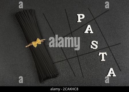 Bunch of black spaghetti on gray background and the word Pasta. Italian cuisine. Stock Photo
