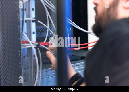 An Expert Engeneer in datacenter server room  connecting cables in server cabinet in network server room. Stock Photo
