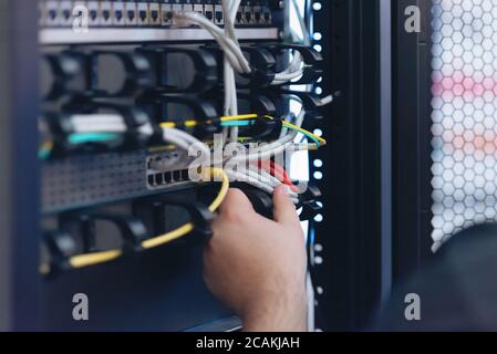 An Expert Engeneer in datacenter server room  connecting cables in server cabinet in network server room. Stock Photo