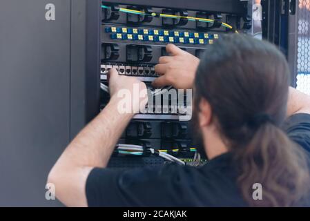 An Expert Engeneer in datacenter server room  connecting cables in server cabinet in network server room. Stock Photo