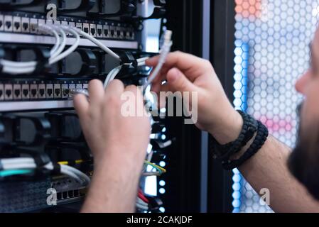 An Expert Engeneer in datacenter server room  connecting cables in server cabinet in network server room. Stock Photo