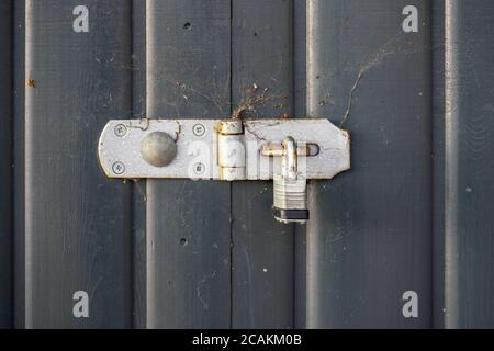 Old padlock, parts covered with rust, on gray wood fence. Stock Photo