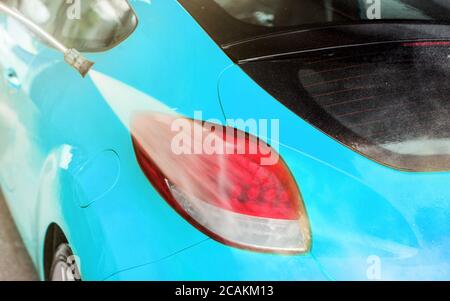 Rear light of blue car washed in self serve car wash, water spraying on the red surface. Stock Photo