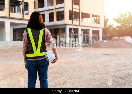 Portrait of an Asian woman engineer construction worker wearing a helmet using a tablet while standing at a construction site. Building Location on th Stock Photo