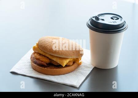 Bacon and Omelette Hamburger on the paper with White paper coffee mug on the table in fast food restaurant Stock Photo
