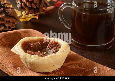 A mini pecan pie or tart with a cup of coffee on a holiday table Stock Photo