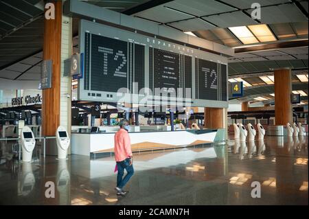 05.08.2020, Singapore, Republic of Singapore, Asia - A man wearing a protective face mask walks past the flight information display inside Terminal 2. Stock Photo