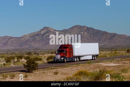Classic big rig heavy duty long haul diesel semi truck with refrigerator semi trailer running on the road along mountains in USA Stock Photo