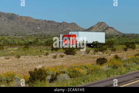 Classic American big rig semi truck with transporting on flat bed semi trailer driving on the road along mountain rock in USA Stock Photo