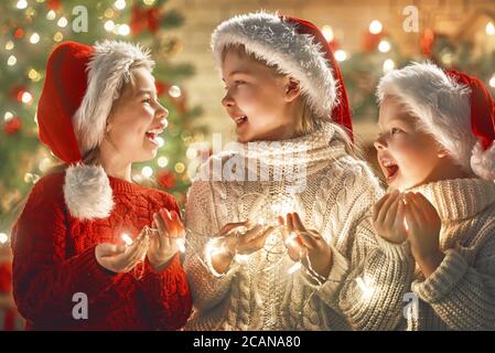 Merry Christmas and Happy Holiday! Cute little children with garland lights near tree at home. Stock Photo