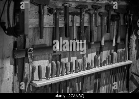Old tools - hammers and files of different sizes on a wooden wall, black and white photo. Stock Photo