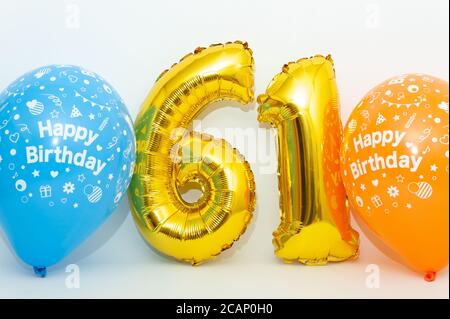 Inflatable numeral 61 sparkling metallic golden color with blue and yellow balloons isolated on white background. Close-up. Horizontal shot. Stock Photo