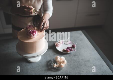 Woman making cake decorating with flower roses staying on kitchen table close up at home. Wedding Day. Selective focus. Stock Photo