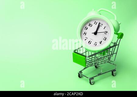 Alarm clock in miniature shopping cart on pink background. Toy trolley on bright colorful background, copy space for text or design. Shopping, purchas Stock Photo