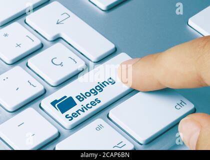Blogging Services Written on Blue Key of Metallic Keyboard. Finger pressing key Stock Photo