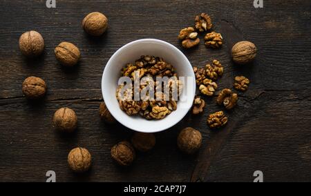 Walnut in a smale plate with scattered shelled nuts and whole nut which standing on a wooden vintage table. Walnuts is a healthy vegetarian protein Stock Photo