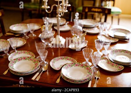 Festive table setting with plates, spoons, knives, glasses, decanters and a candlestick in the center on a wooden table. Stock Photo