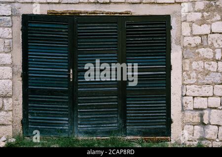 An old closed window in black with a blue tint with blinds on a brick wall. Stock Photo