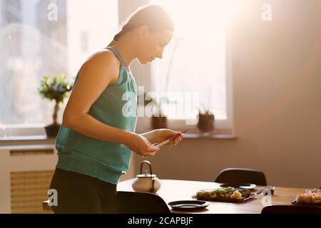 Young woman waiting for guests, friends while arranging the table with various sushi sets in a sunny home with window in the background Stock Photo
