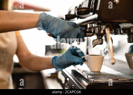 Young woman making coffee espresso while wearing surgical mask and gloves for preventing corona virus spread - Bar owner safety working Stock Photo