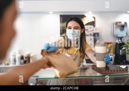 Bar owner working only with take away orders during corona virus outbreak - Young woman worker wearing face surgical mask giving takeout meal