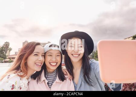 Happy Asian girls taking selfie with mobile smartphone outdoor - Young trendy social friends having fun using new technology apps Stock Photo