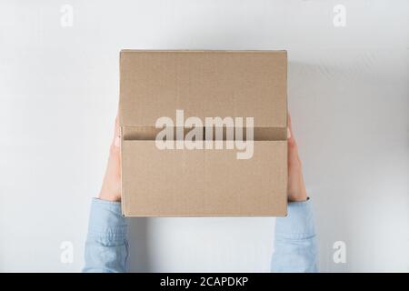 Large square cardboard box in female hands. Top view, white background Stock Photo