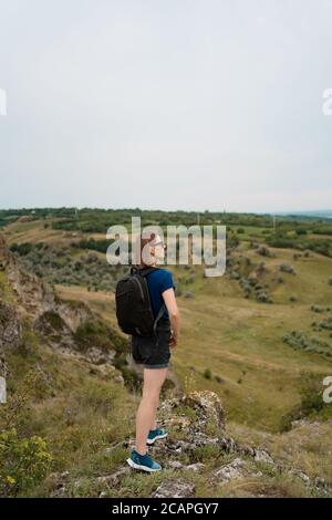 Young woman with backpack standing on cliff's edge and looking to the sky and beautiful nature. Discover wild places. Internal tourism Stock Photo