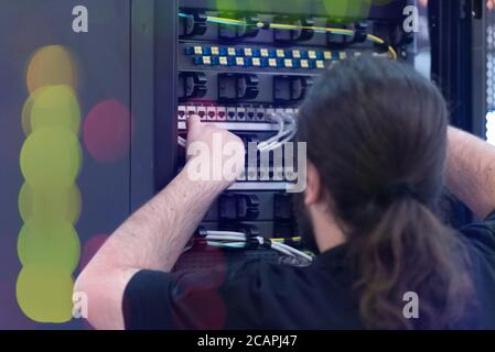 An Expert Engeneer in datacenter server room  connecting cables in server cabinet in network server room. Stock Photo