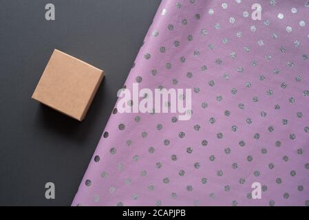 Small cardboard box and lilac polka dot wrapping paper. Gray table. Preparation for the holiday Stock Photo