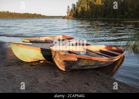 Old shabby wooden fishing colorful boats on the lake shore during sunset, autumn forest on background. Calm sunset on the nature Stock Photo