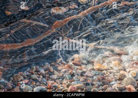 Beach stones, receding water and rockface with igneous dyke, Lake Superior Provincial Park, Ontario, Canada Stock Photo