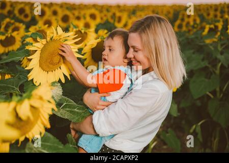 Mother with little baby son in sunflowers field during golden hour Stock Photo