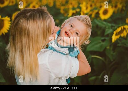 Mother with little baby son in sunflowers field during golden hour Stock Photo