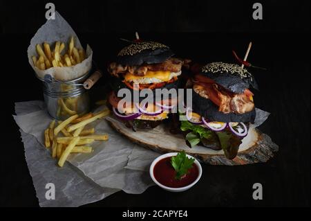 two huge black burgers with fries and tomato sauce on a dark background Stock Photo