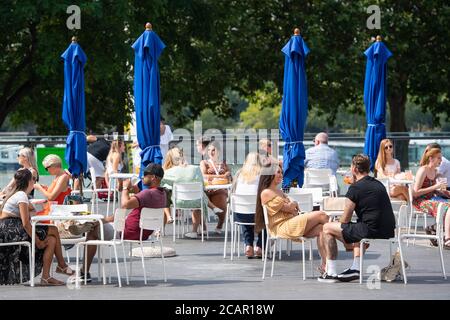 People enjoy the hot weather at tables outside a bar on the South Bank, in central London. Stock Photo