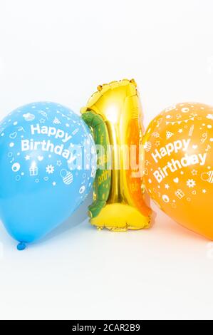 Inflatable numeral 1 sparkling metallic golden color with blue and yellow balloons isolated on white background. Close-up. Copy space. Vertical shot. Stock Photo