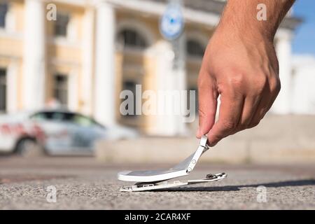Male hands holding broken mobile smartphone after drop, view from above, outdoors. Smart phone with broken (cracked) screen. Stock Photo