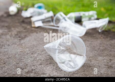 Heap of rubbish on the path, closeup. Empty used plastic cups and plastic bottles on blurred background, selective focus.Environmental pollution Stock Photo