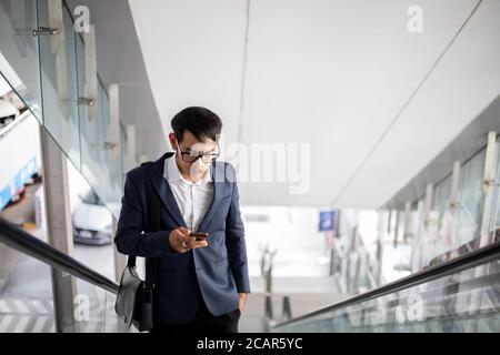Asian businessmen are using their phones and going up the escalator to work in the morning. Stock Photo