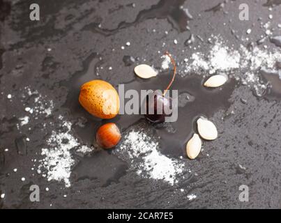 Colour Photograph of Wet Cherries seeds and nuts on black slate Stock Photo